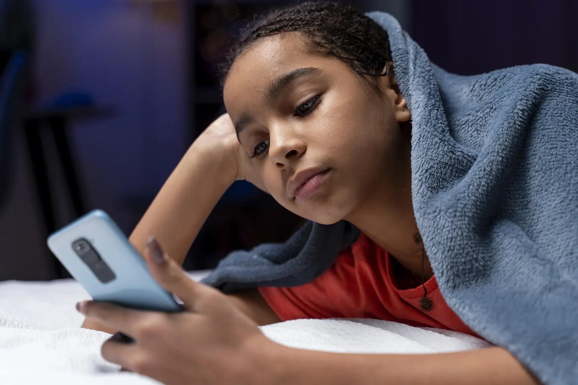 Teenage girl using mobile phone under blanket